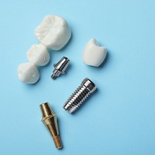 Dental implant posts, abutment, crown, and bridge on a light blue surface