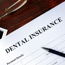 Closeup of a dental insurance form with pen, X-rays, glasses, and money