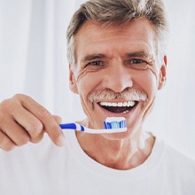 older man in white t-shirt brushing his teeth