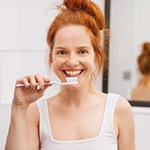 Woman smiles while brushing to prevent dental emergencies in Virginia Beach
