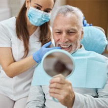 dentist smiling while looking in dental mirror  