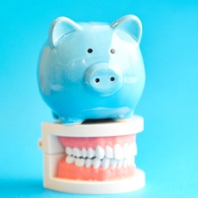 Blue piggy bank atop model teeth representing cost of veneers in Virginia Beach