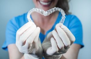 dental team member holding two clear aligners in the shape of a heart 