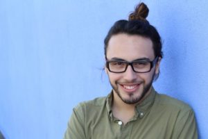 man with small teeth smiling in front of a blue background 