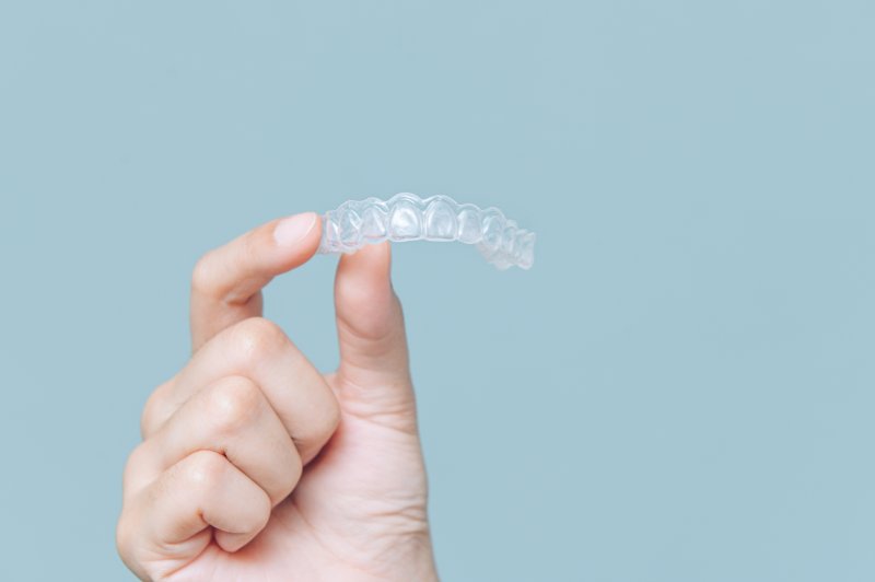 Hand holding clear aligner over light blue background