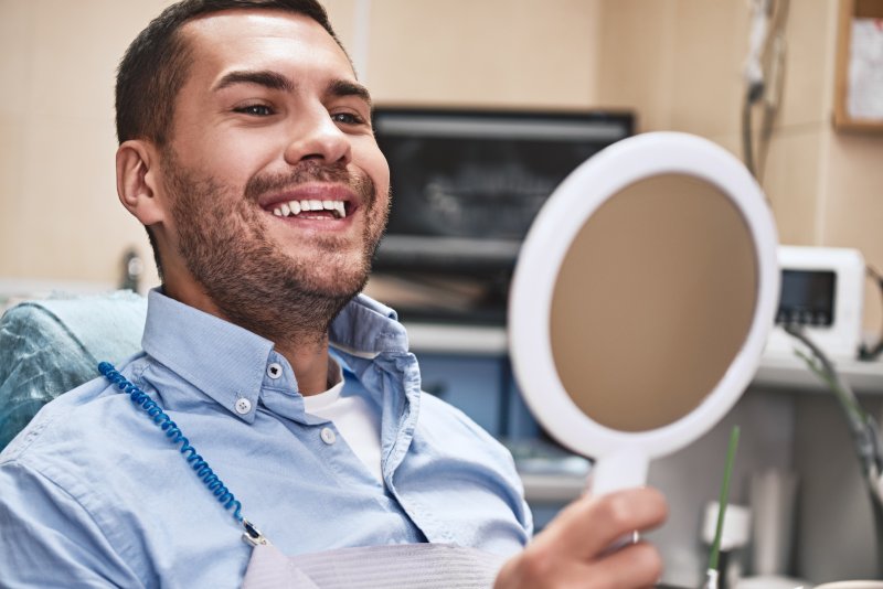 A man admiring his new dental crown in a hand mirror